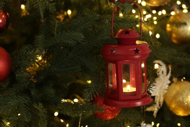 Christmas lantern with burning candle on fir tree as background, closeup