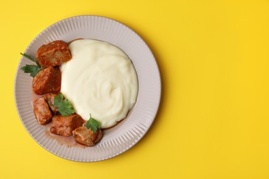 Delicious goulash with mashed potato on yellow background, top view. Space for text