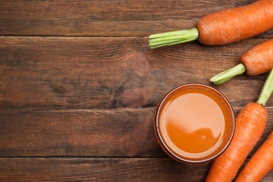 Flat lay composition with carrots and juice on wooden table, space for text