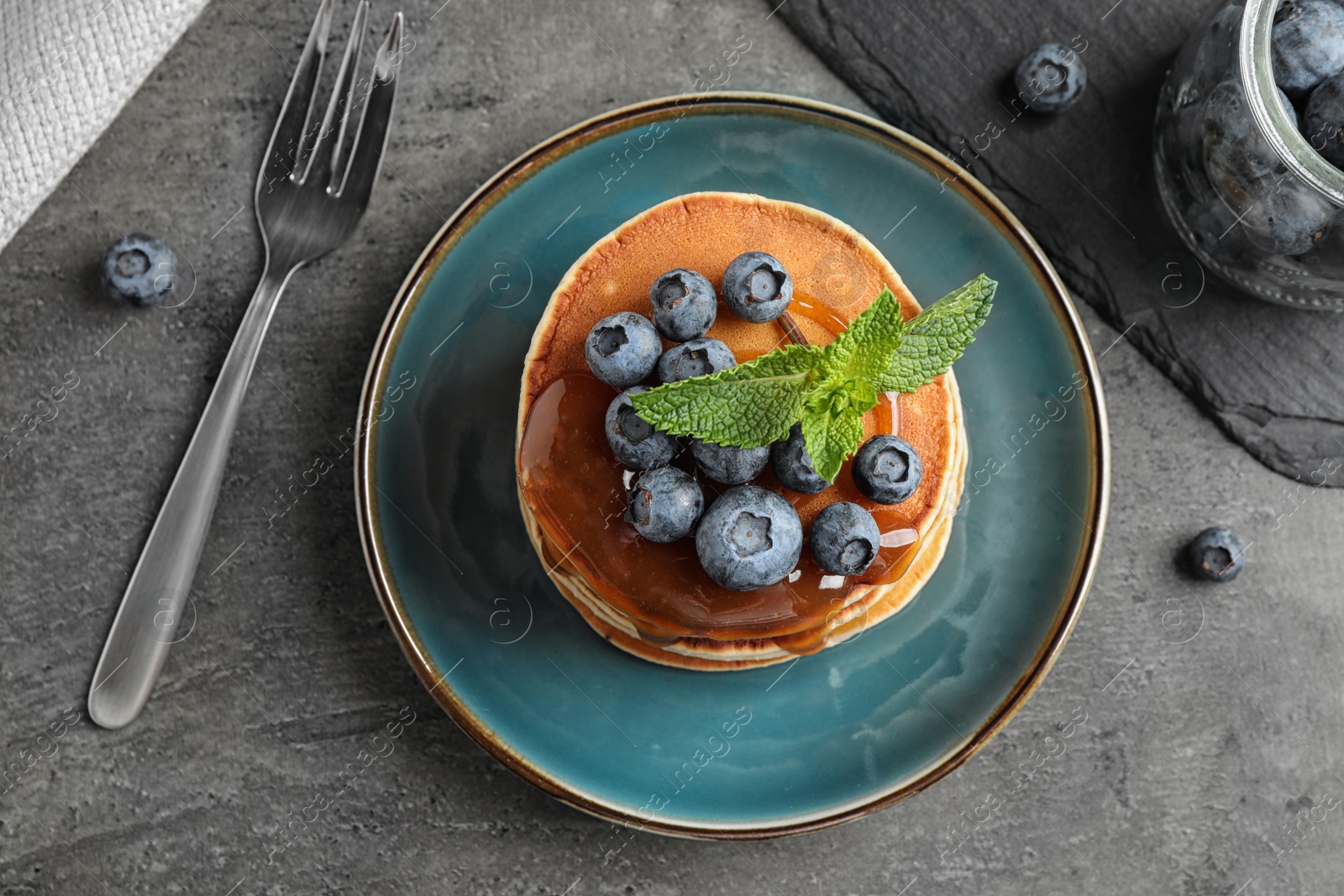 Photo of Tasty pancakes and blueberries served on grey table, flat lay