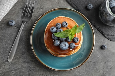 Tasty pancakes and blueberries served on grey table, flat lay