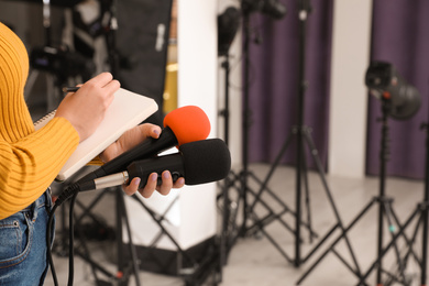 Professional journalist with microphones taking notes indoors, closeup