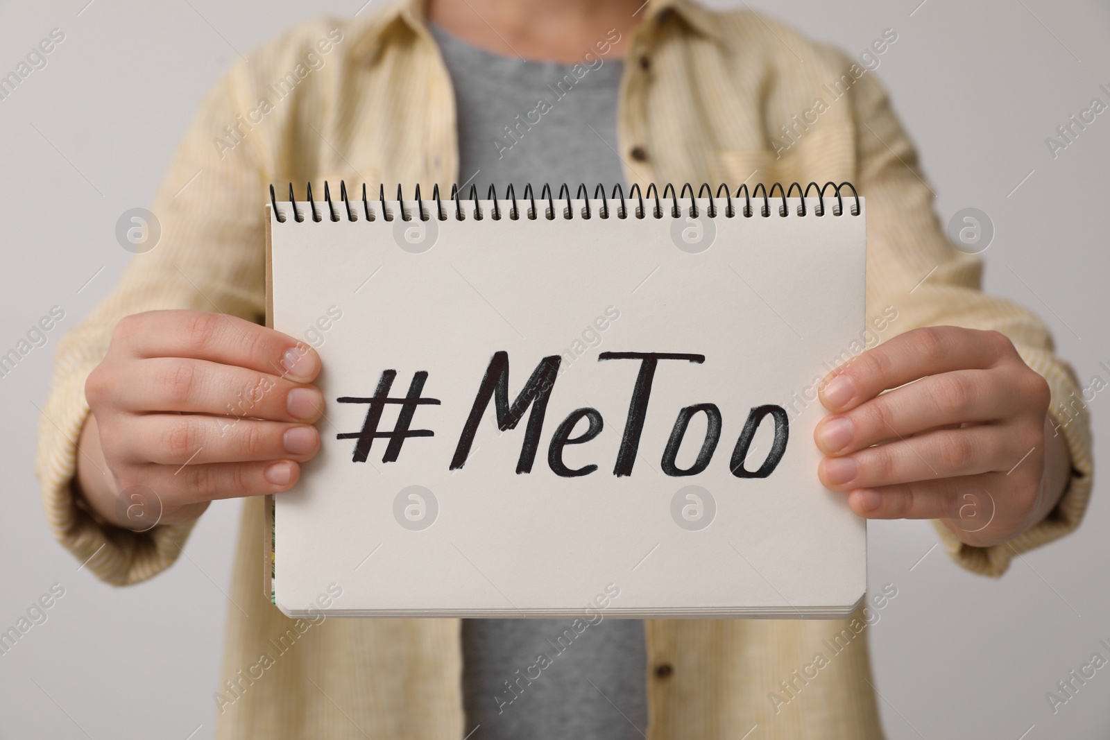 Photo of Woman holding notebook with hashtag MeToo against light background, closeup. Stop sexual assault