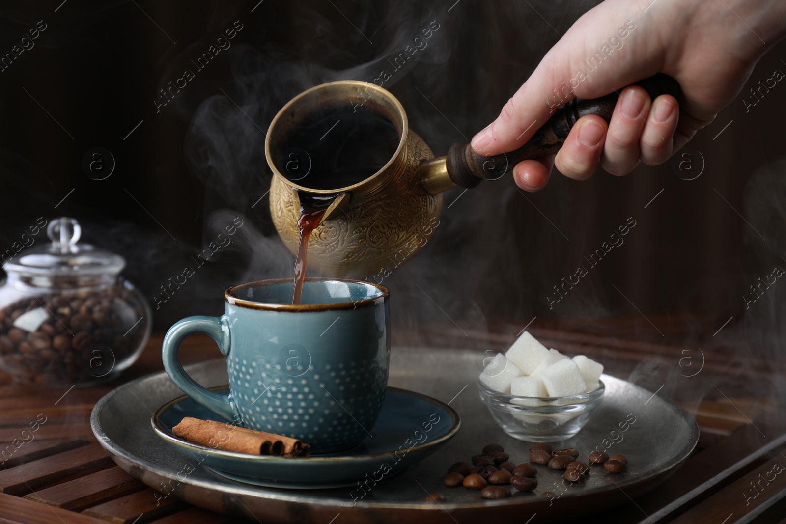 Photo of Turkish coffee. Woman pouring brewed beverage from cezve into cup at wooden table, closeup