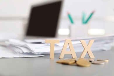 Photo of Word TAX and coins on table against blurred background