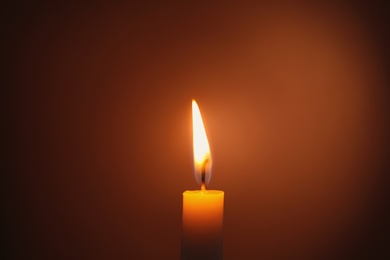 Photo of Wax candle burning in darkness, closeup