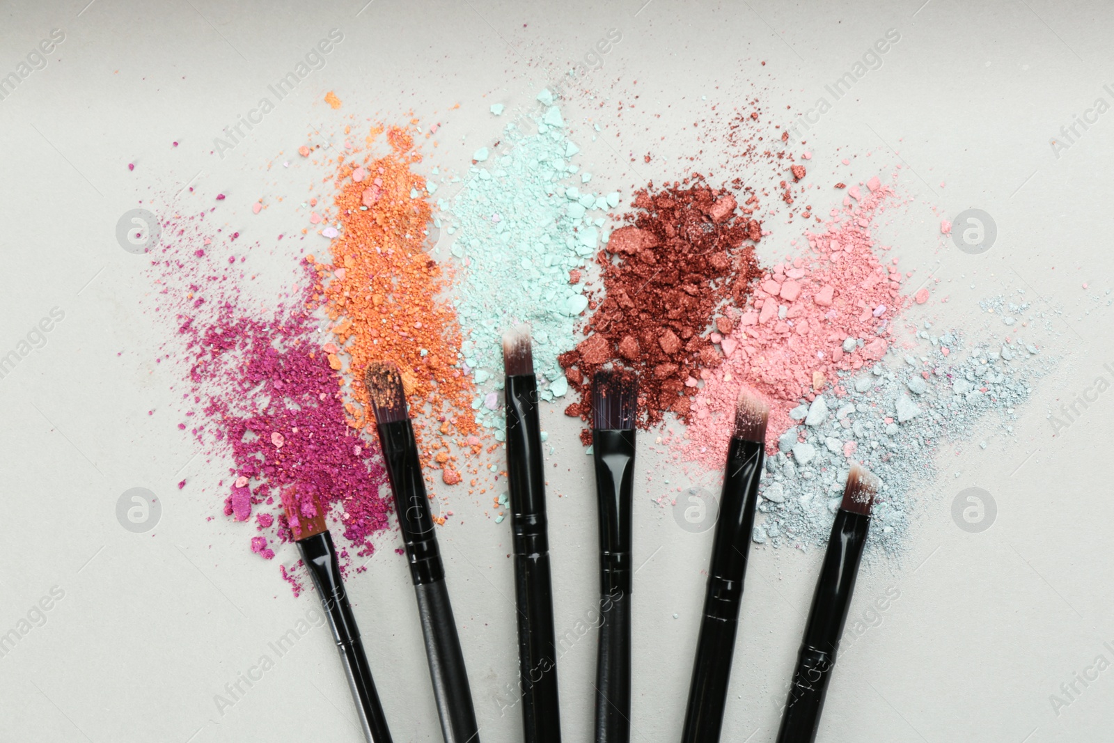 Photo of Makeup brushes and scattered eye shadows on light grey background, flat lay