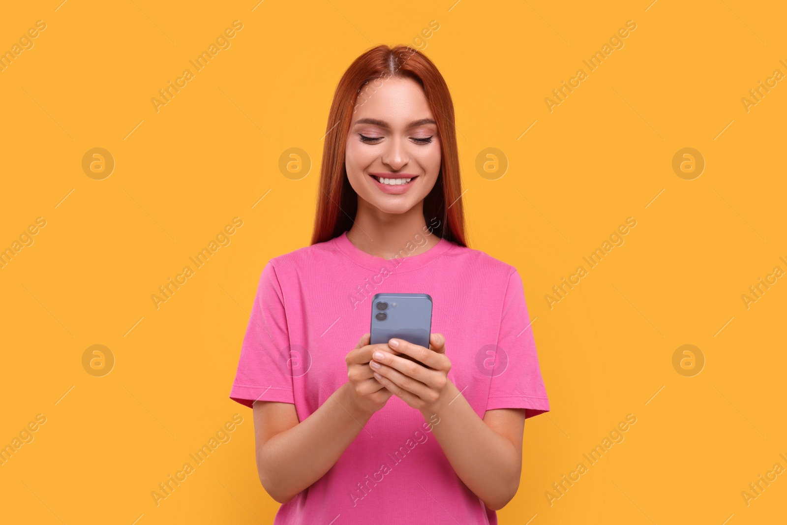 Photo of Beautiful happy woman using smartphone on orange background