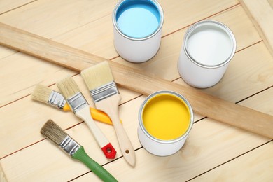 Cans of colorful paints and brushes on wooden table, above view