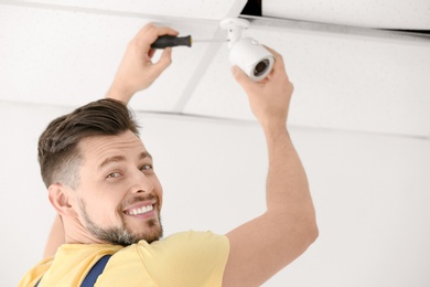 Technician installing CCTV camera on ceiling indoors