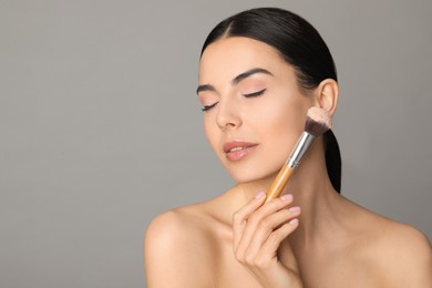 Photo of Beautiful young woman applying face powder with brush on grey background. Space for text