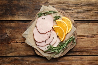 Photo of Delicious cut ham with rosemary, peppercorns and orange slices served on wooden table, top view