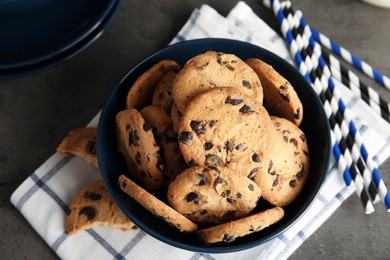 Photo of Bowl with tasty chocolate chip cookies on grey table, top view