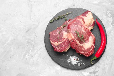 Photo of Fresh raw beef cut with different spices on light grey textured table, top view. Space for text