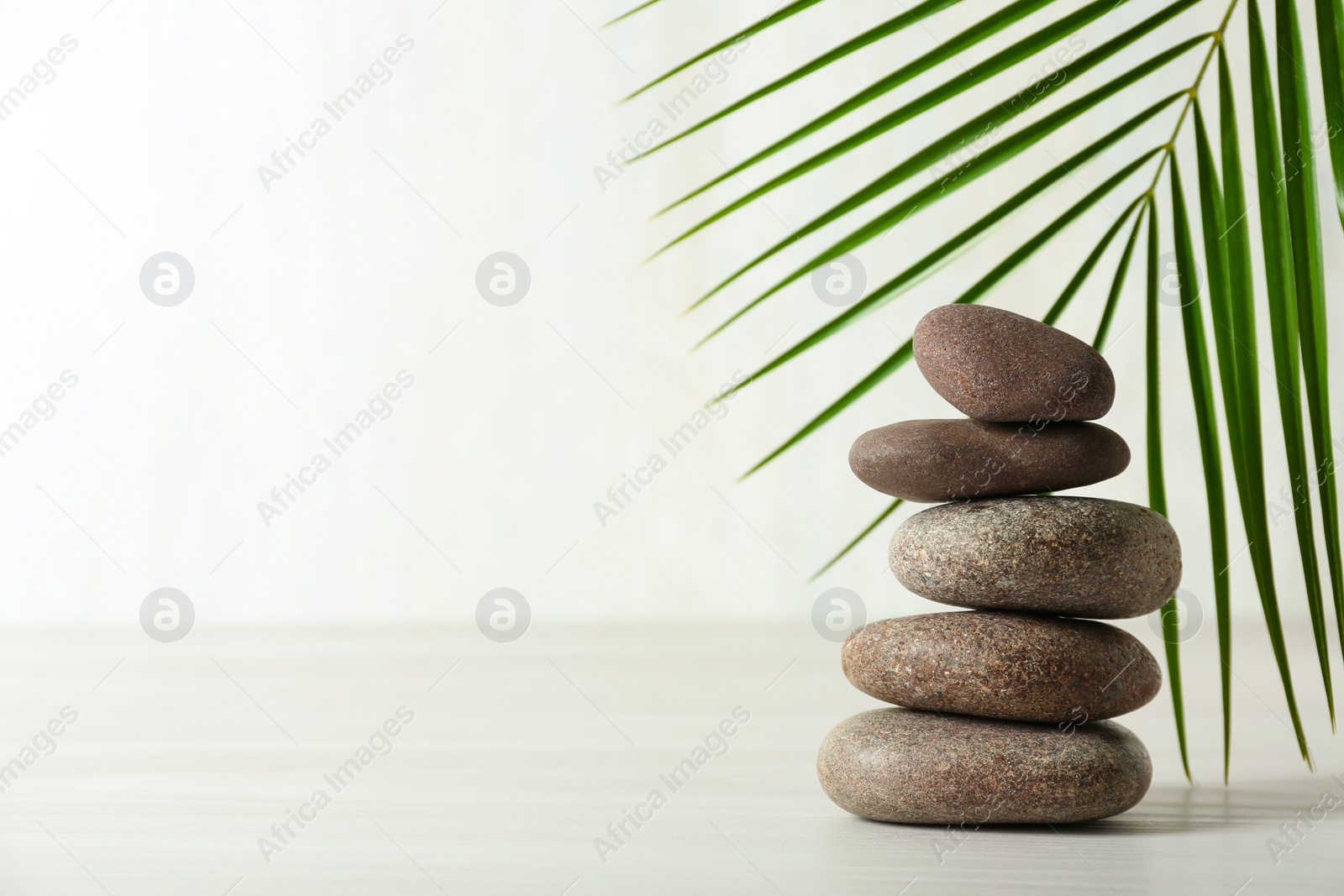 Photo of Stack of spa stones and palm leaf on table against white background, space for text