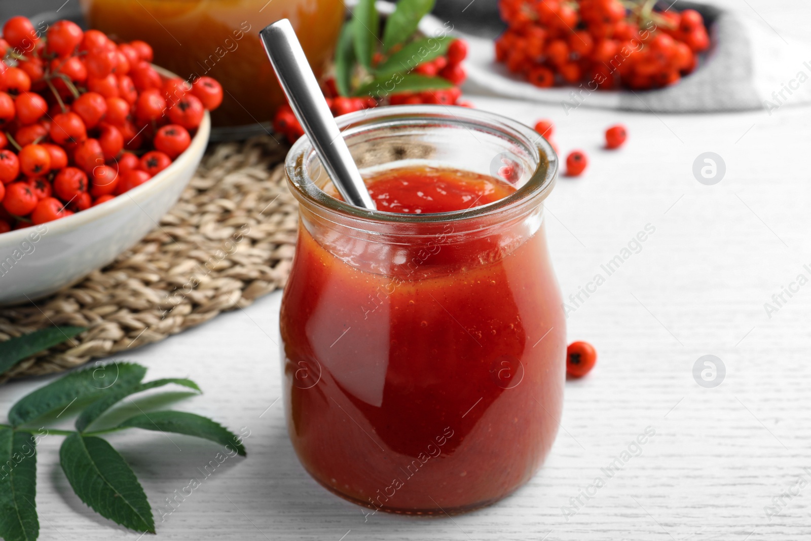 Photo of Delicious rowan jam in glass jar on white wooden table