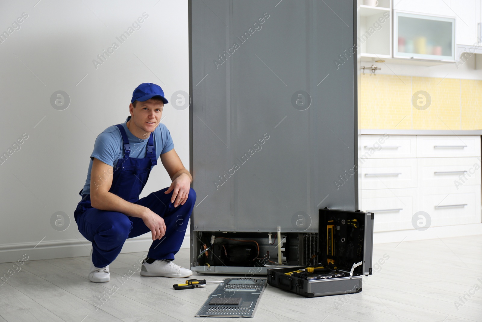 Photo of Male technician in uniform near broken refrigerator indoors