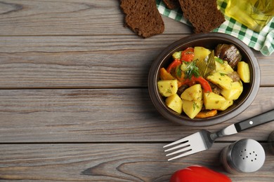 Tasty cooked dish with potatoes in earthenware served on wooden table, flat lay. Space for text