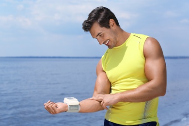 Photo of Young man checking pulse with medical device after training on beach