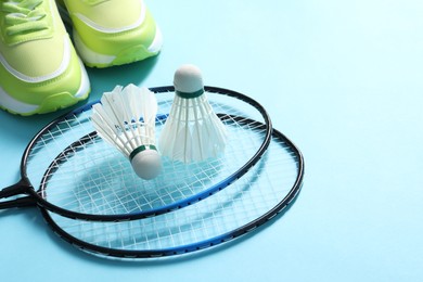 Photo of Feather badminton shuttlecocks, rackets and sneakers on light blue background, space for text