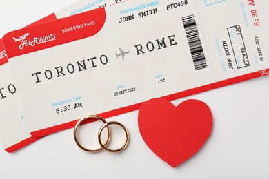 Honeymoon concept. Plane tickets, red paper heart and two golden rings on white background, top view