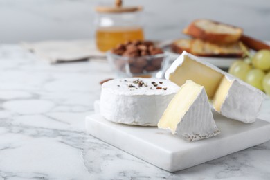 Photo of Tasty brie cheese on white marble table, space for text