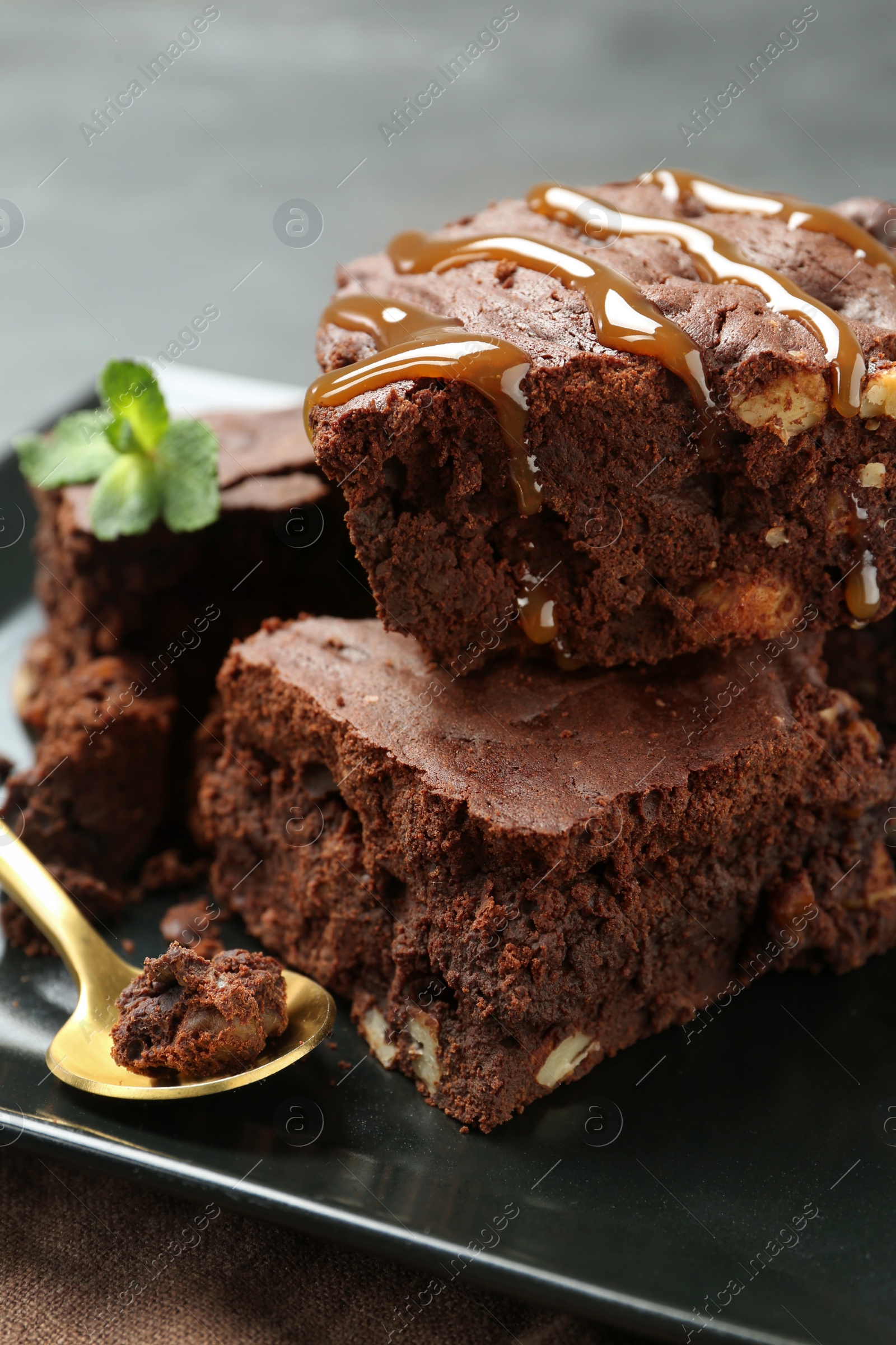 Photo of Delicious chocolate brownies with nuts, caramel sauce and fresh mint on plate, closeup