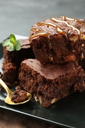 Photo of Delicious chocolate brownies with nuts, caramel sauce and fresh mint on plate, closeup