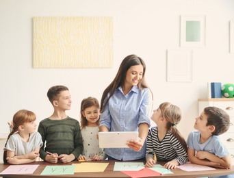 Photo of Cute little children with teacher in classroom at school