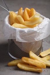 Photo of Frying basket with tasty french fries on light grey table, closeup