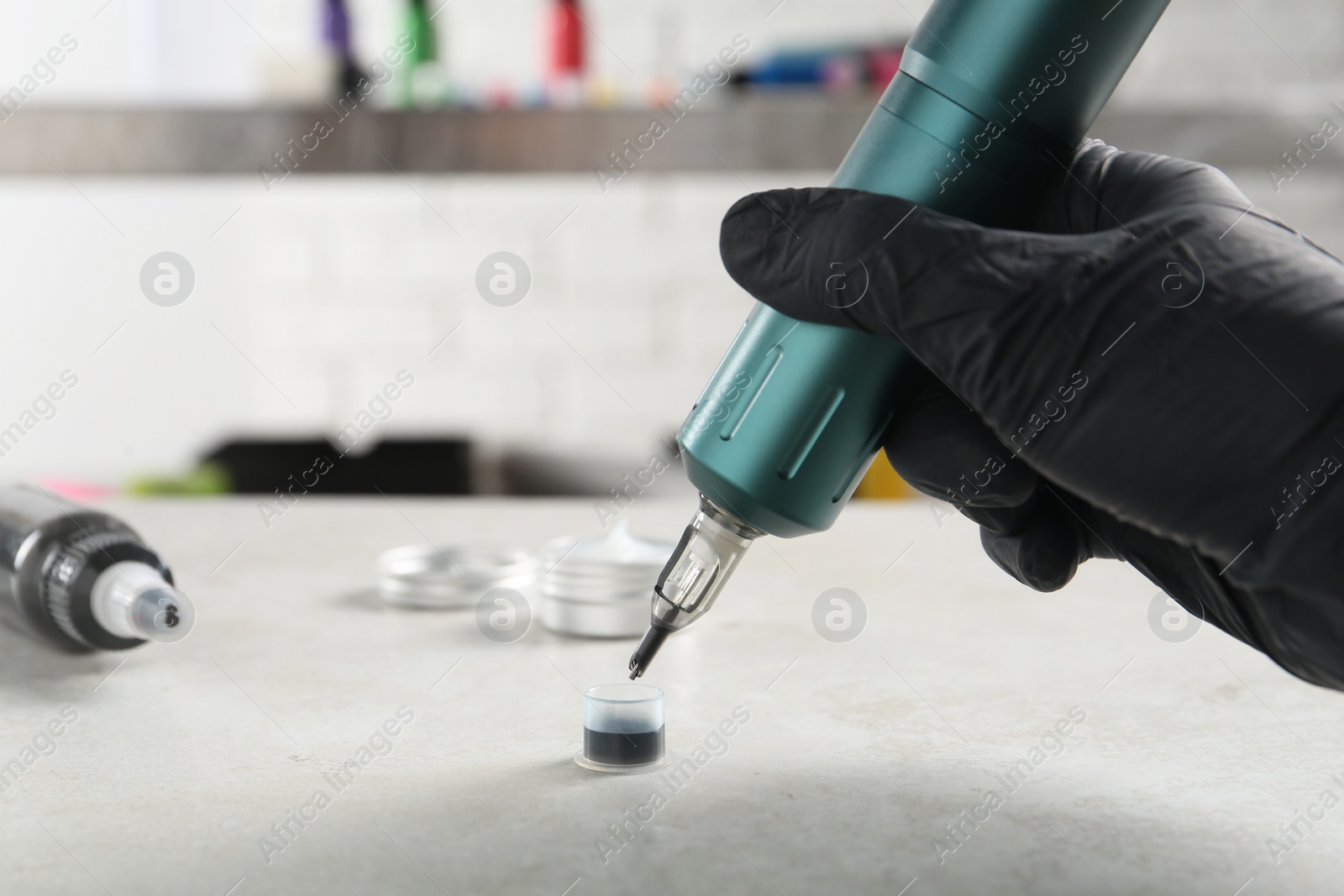 Photo of Tattoo artist with professional machine and ink at white table in salon, closeup