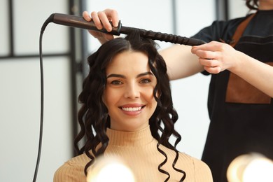 Hair styling. Hairdresser curling woman's hair in salon, closeup