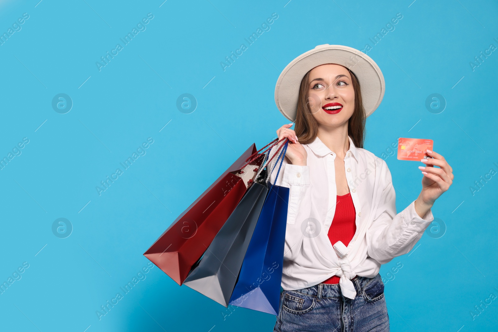 Photo of Stylish young woman with shopping bags and credit card on light blue background, space for text