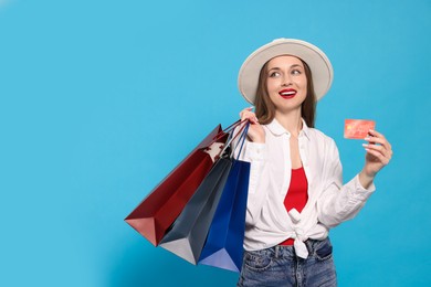 Stylish young woman with shopping bags and credit card on light blue background, space for text