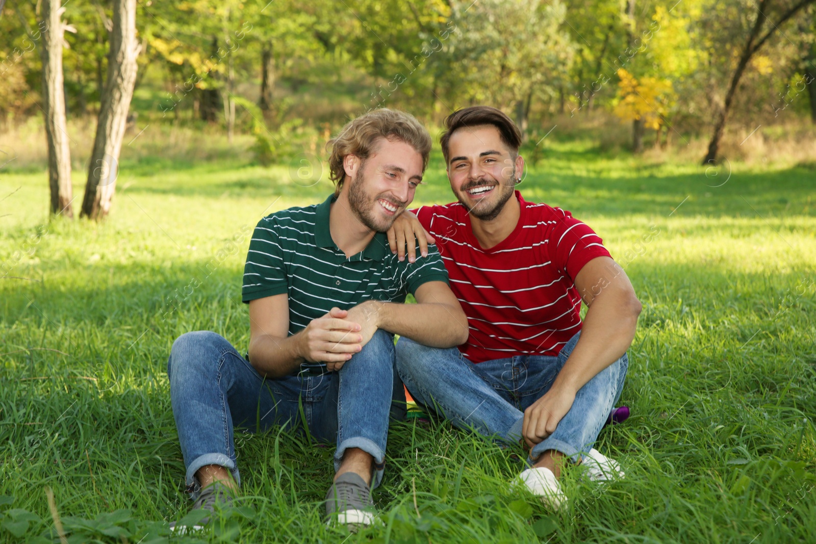 Photo of Portrait of happy gay couple sitting on grass in park