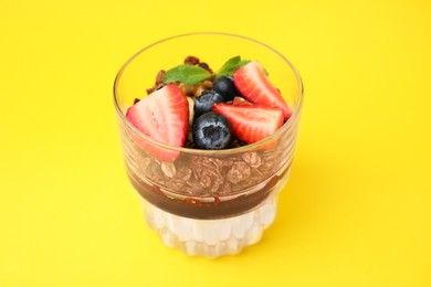 Photo of Tasty granola with berries, jam and yogurt in glass on yellow background, closeup