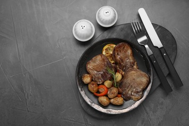 Tasty beef tongue pieces, rosemary, lemon and potatoes on grey table, flat lay. Space for text