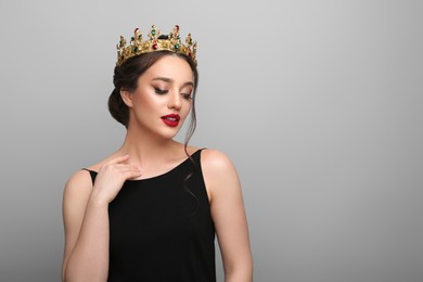 Beautiful young woman wearing luxurious crown on light grey background, space for text