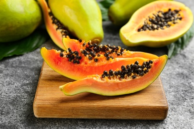 Fresh ripe papaya fruits with green leaves on grey table