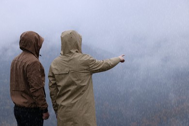 Photo of Man and woman in raincoats enjoying mountain landscape under rain