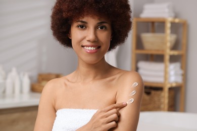 Photo of Beautiful young woman applying body cream onto arm in bathroom