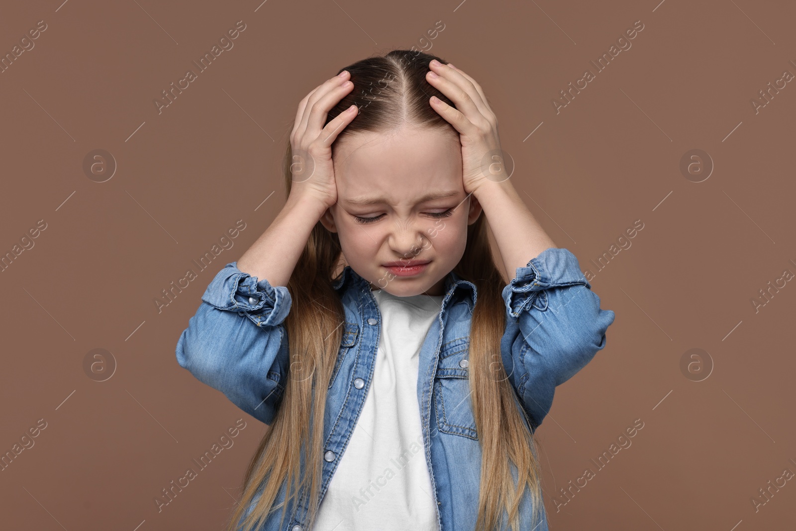 Photo of Little girl suffering from headache on brown background