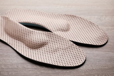 Beige orthopedic insoles on wooden background, closeup