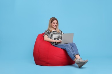 Happy woman with laptop sitting on beanbag chair against light blue background
