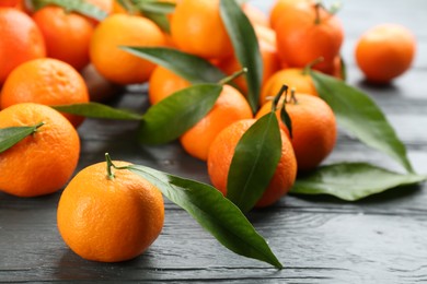 Photo of Fresh ripe tangerines with green leaves on grey wooden table