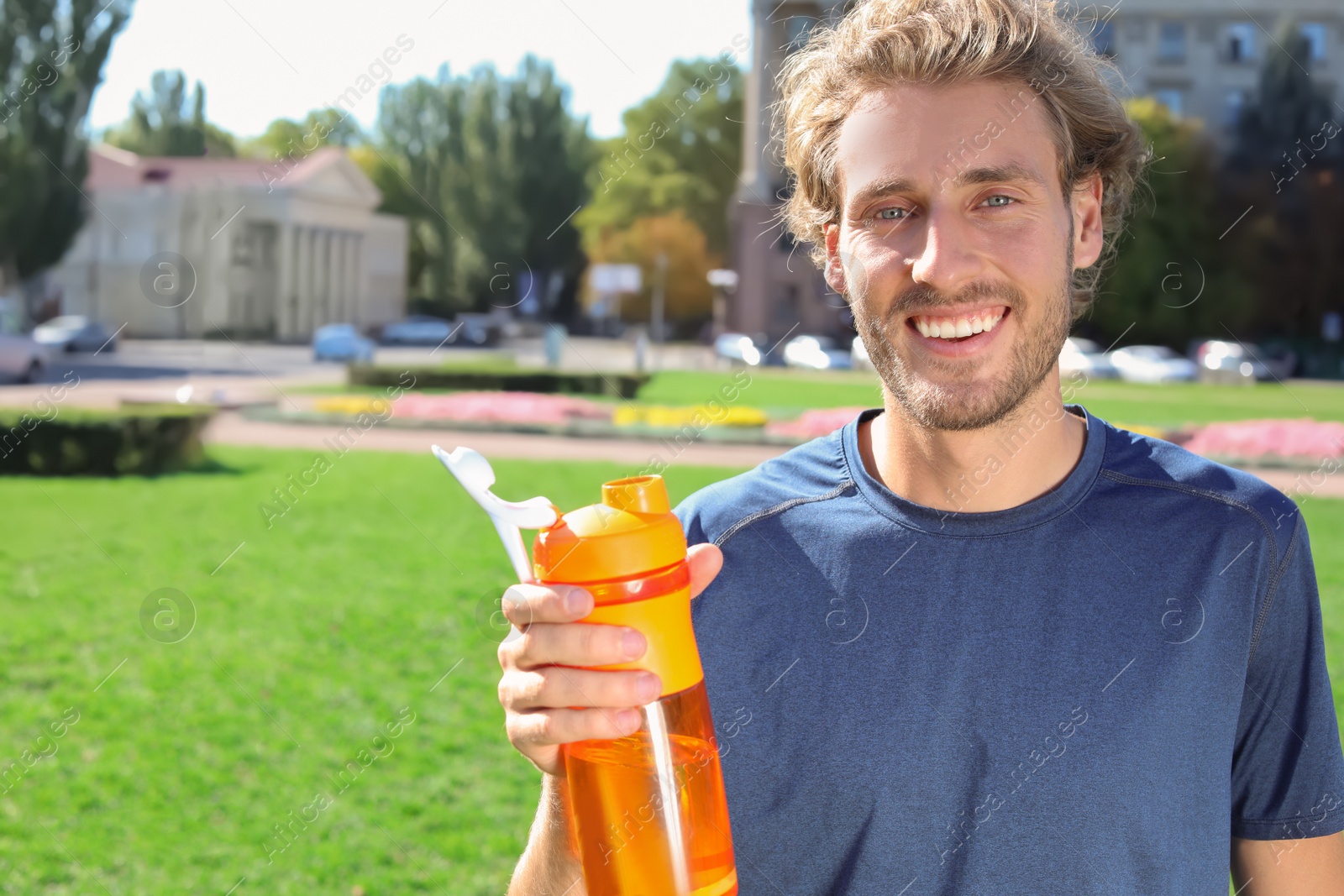 Photo of Young man holding bottle with clean water on city street. Space for text