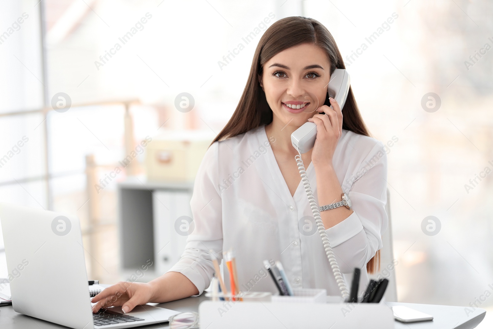 Photo of Young woman talking on phone at workplace