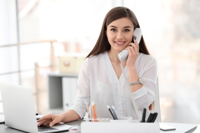 Photo of Young woman talking on phone at workplace