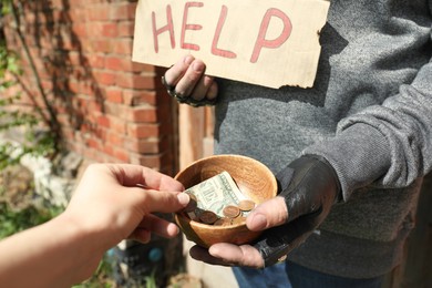 Photo of Woman giving money to poor homeless man with Help sign outdoors, closeup. Charity and donation
