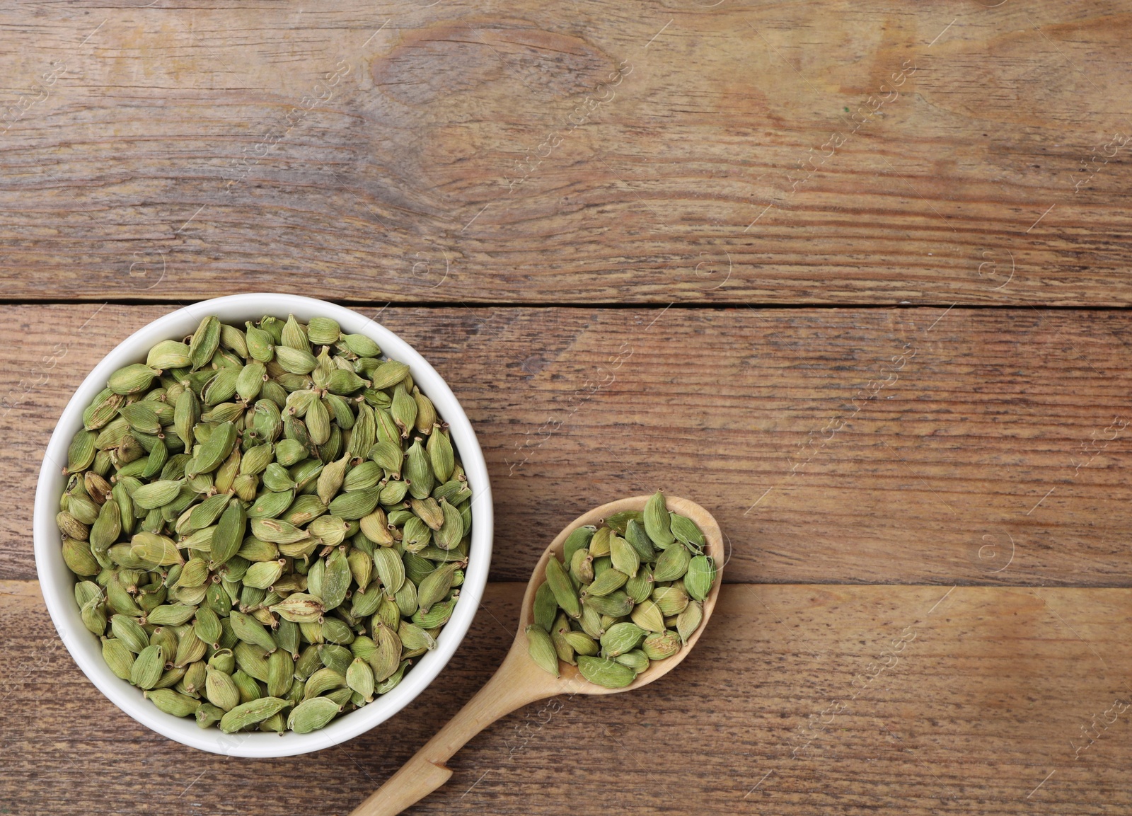 Photo of Bowl and spoon with dry cardamom pods on wooden table, flat lay. Space for text